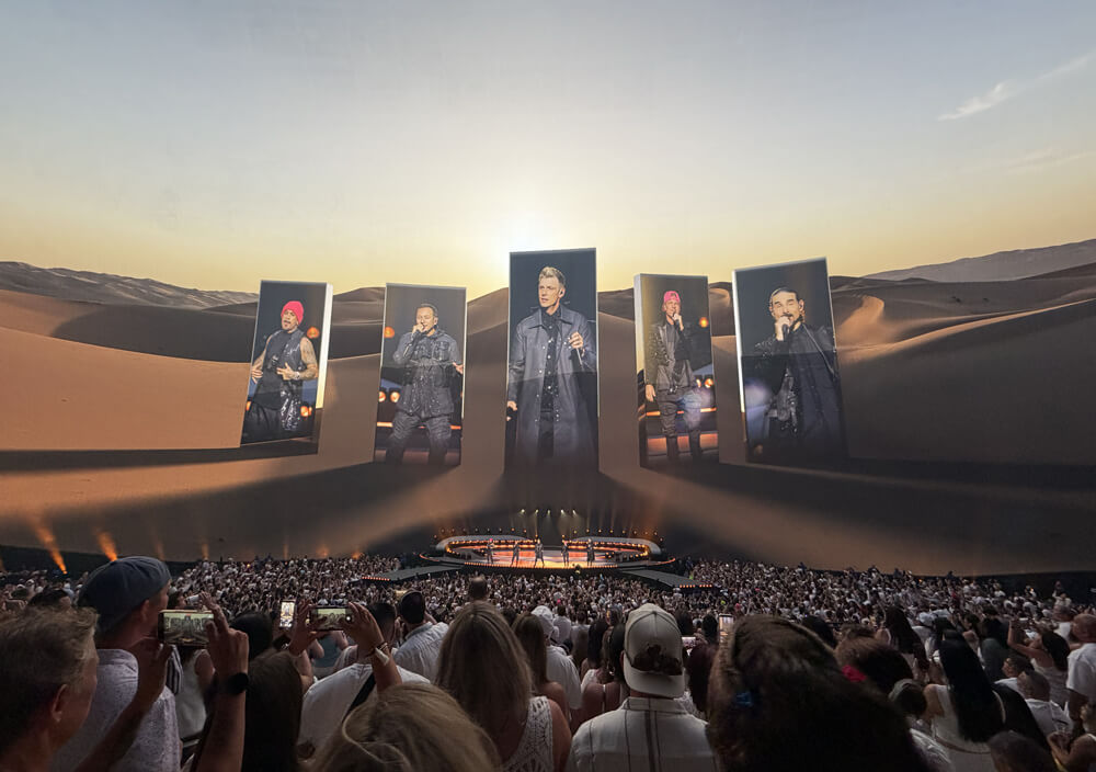 Backstreet Boys on stage, big desert scene on screen with “portals” showing video of the guys