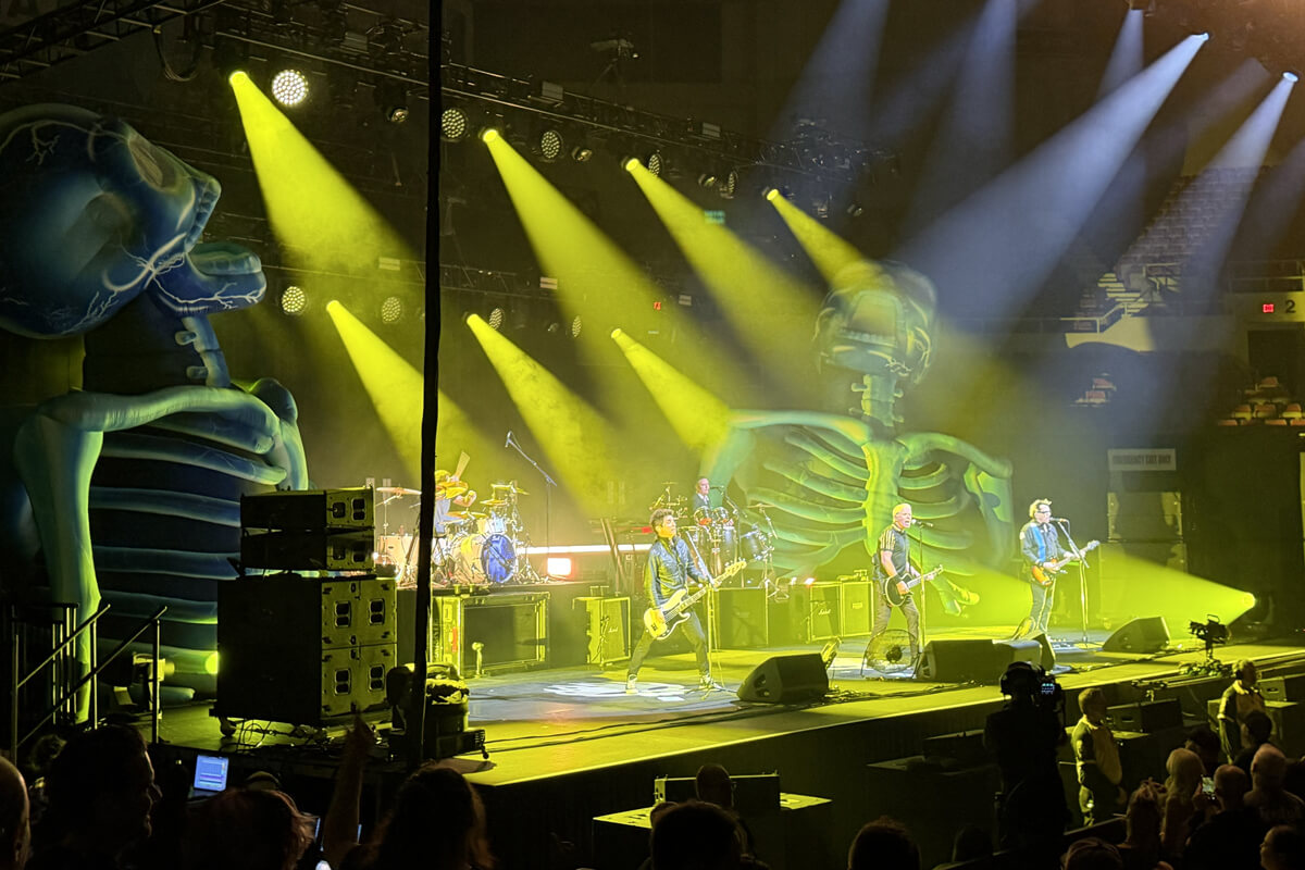 The Offspring on stage bathed in yellow light and flanked by two giant skeleton inflatables