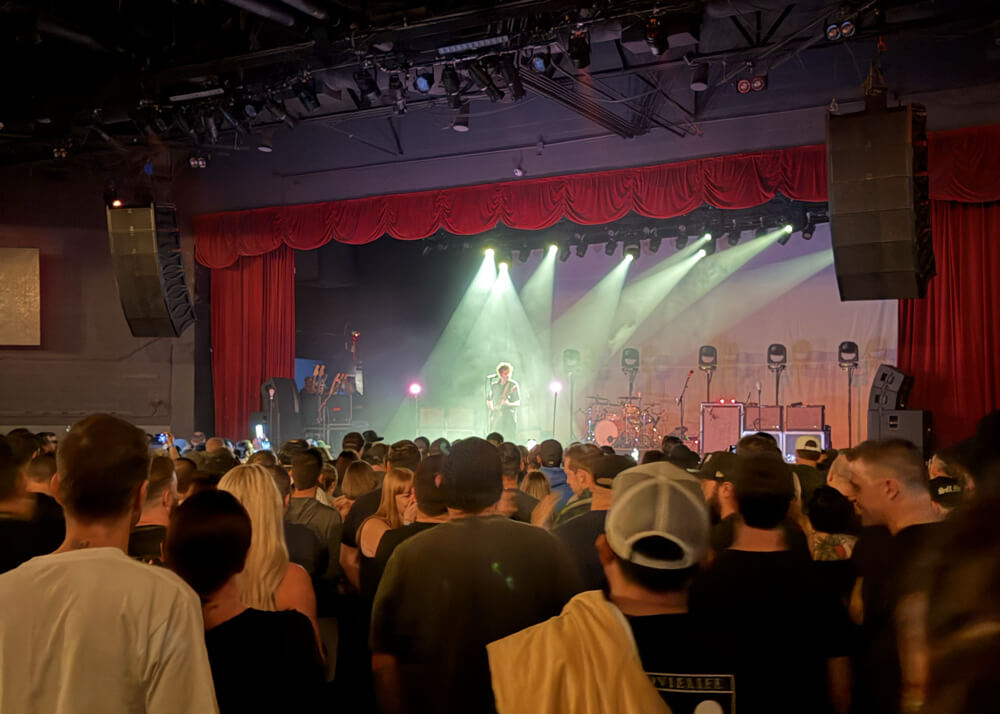 Kenny Vasoli in spotlight on stage, the audience is well lit